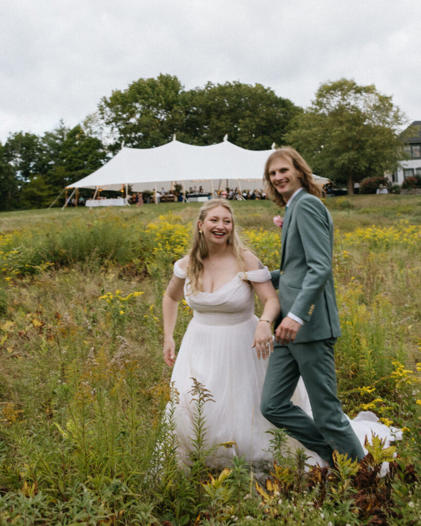 Couple runs through meadow in the backyard of their parents land turned wedding venue